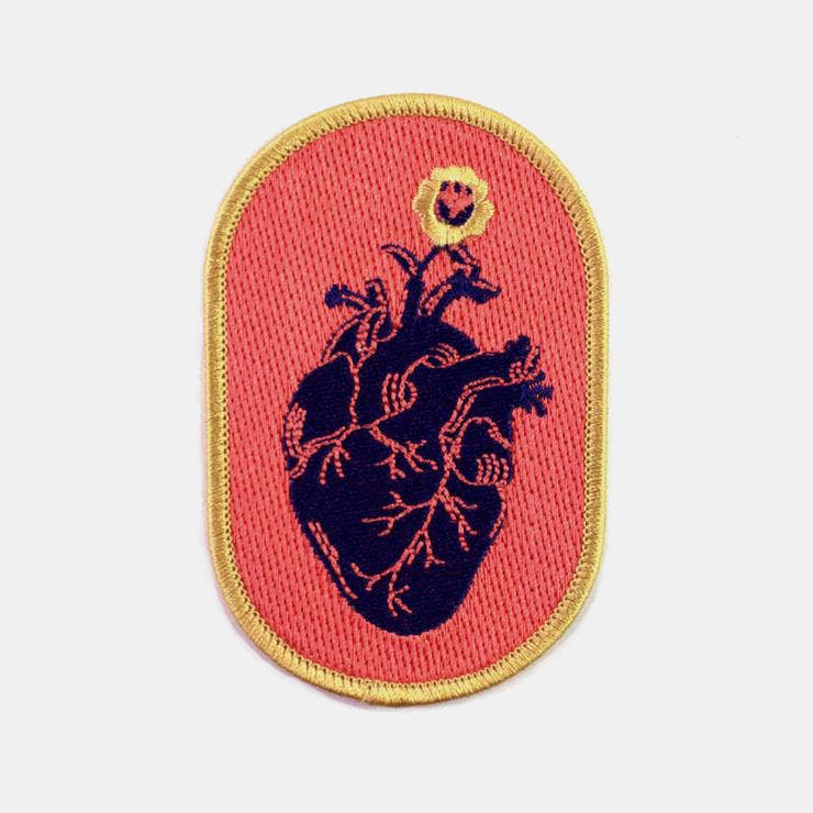 Oblong embroidered patch with an illustration of a navy blue anatomical heart on a coral background with yellow border 