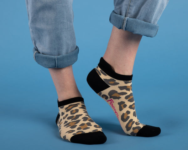Leopard print ankle socks with black toes, cuffs, and heels. Shown worn by a model in front of a blue background 