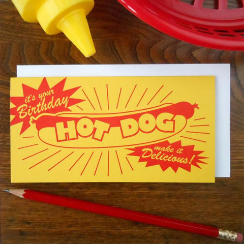 Rectangular yellow letterpress greeting card with illustration of a hot dog and message “It’s your birthday, make it delicious!” in bright red