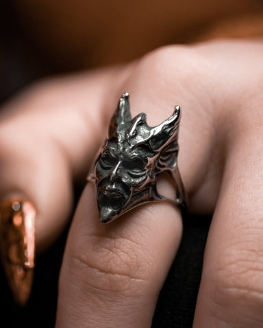 Model wearing stainless steel ring in the shape of a demon with pointed horns and face in angry expression with closed mouth. Seen from the left side angle