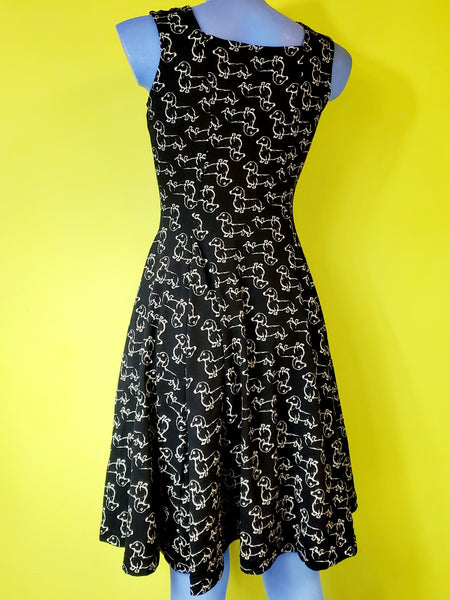 sleeveless stretch cotton knit flared knee length dress with sweetheart neckline in a cream print repeat pattern of dachshunds against a black background. back view shown worn by a mannequin