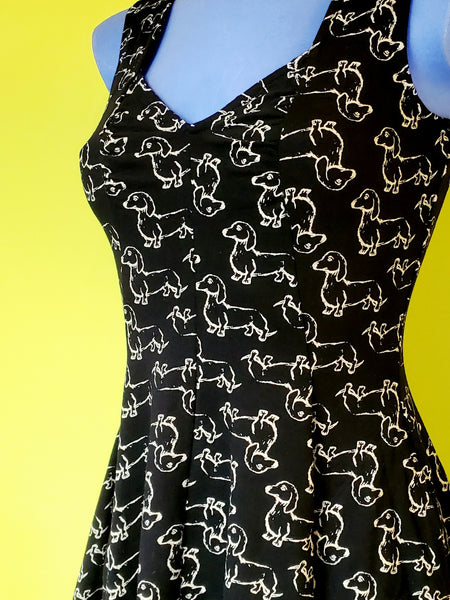 sleeveless stretch cotton knit flared knee length dress with sweetheart neckline in a cream print repeat pattern of dachshunds against a black background. close up view shown worn by a mannequin