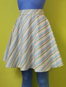 A cotton skater style mini skirt with a wide waistband and a diagonal rainbow stripe pattern on a white background. shown on a mannequin