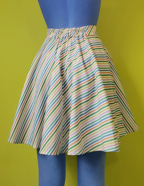 A cotton skater style mini skirt with a wide waistband and a diagonal rainbow stripe pattern on a white background. shown back view on a mannequin