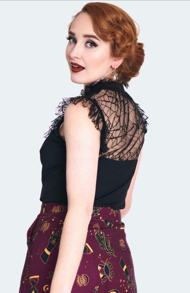 A model wearing a black sleeveless spider patterned lace top with a solid black knit bodice. It has a high frilly lace neck and matching black tie at the collar with a keyhole detail. Shown from back