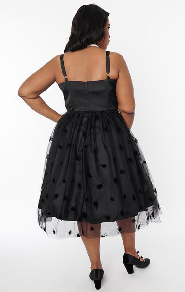 A model wearing a black swing dress with a sweetheart neckline, princess seaming, and matching spaghetti straps. The skirt is full and just below the knee and has a black tulle overlay with an all-over pattern of flocked black cockroaches. Seen from back