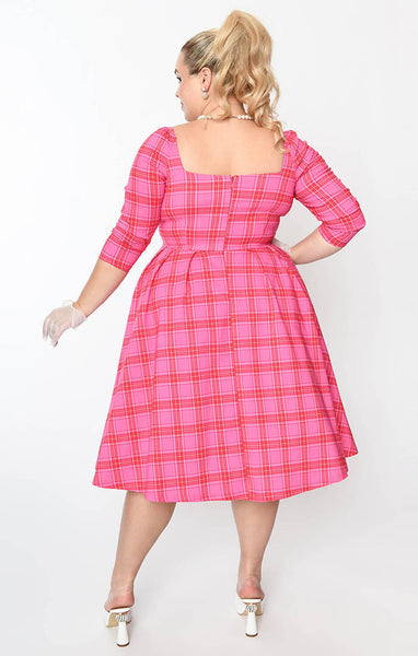 Plus size model wearing a swing dress in a pink, red, and white plaid pattern with 3/4 sleeves, sweetheart neckline with button detail, open square back, and a full knee length skirt. Shown from the back