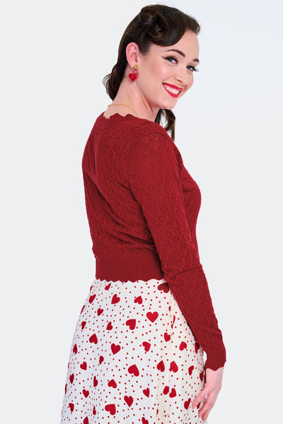 Model wearing deep red v-neck cardigan with openwork heart design, scalloped edges, and black plastic heart-shaped buttons. Shown from the back buttoned up
