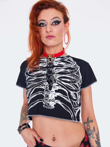 Model wearing a cropped black t-shirt with a white screen printed image of a skeleton’s ribs on the front. Shirt has raw edge with white thread serged edges. Seen from front