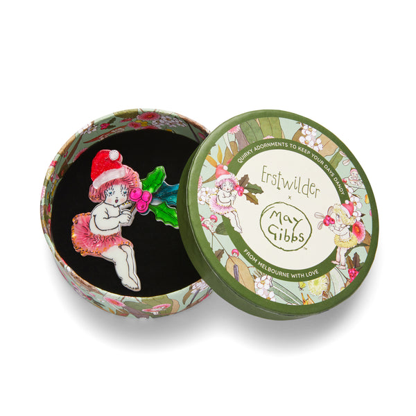 May Gibbs Christmas Collection "Little Ragged Christmas Blossom" layered resin seated gumnut baby in santa hat holding holly sprig brooch, shown in illustrated round box packaging