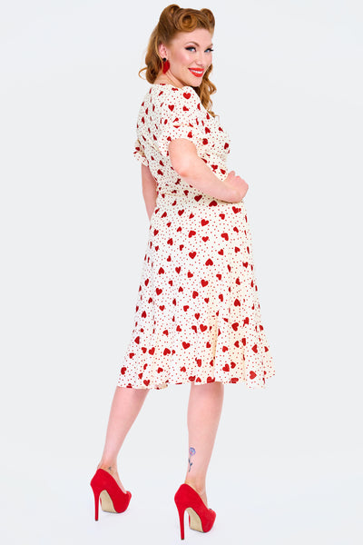 retro style short sleeve knee length wrap dress in red hearts & polka dots print on a cream background print. showing 3/4 back view worn by a model.