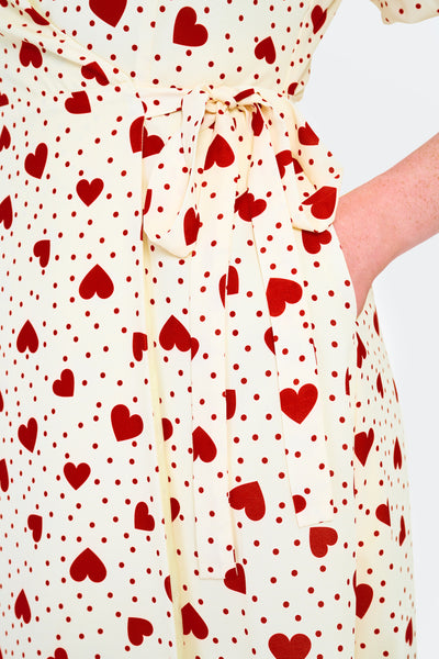 retro style short sleeve knee length wrap dress in red hearts & polka dots print on a cream background print. shown close up of waist and side seam pocket worn by a model.