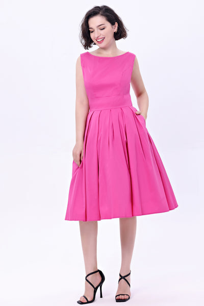 Model wearing a hot pink fit and flare dress made of soy silk. It has a high fitted neckline, princess seamed bodice, wide banded waist, and box pleated knee length skirt with pockets. Shown from the front