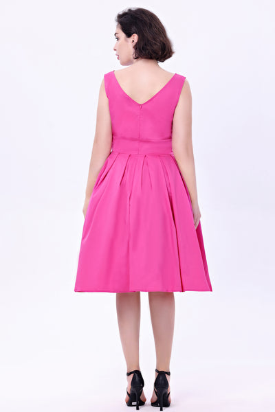 Model wearing a hot pink fit and flare dress made of soy silk. It has a high fitted neckline, princess seamed bodice, wide banded waist, and box pleated knee length skirt with pockets. Shown from the back