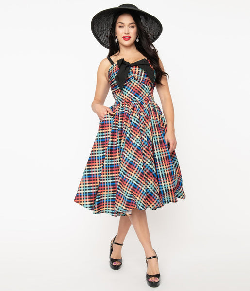 rainbow madras plaid 50s style fit & flare silhouette sundress featuring a princess-seamed bodice with ruched bust sweetheart neckline, applied big black bow and elasticized smocked back panels, removable adjustable straps, and a full swing skirt with side seam pockets in a below the knee length, shown on model
