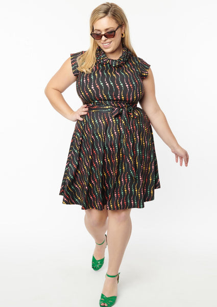 A fit and flare dress with a cowl neck and cap sleeves. It has a pattern of swirled dots in red, green, yellow, and blue on a black background. Shown on a model 