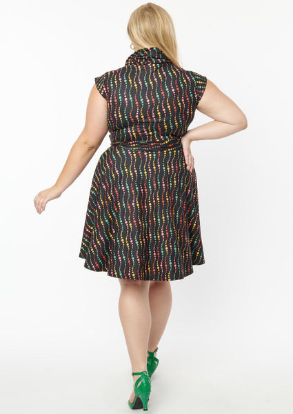 A fit and flare dress with a cowl neck and cap sleeves. It has a pattern of swirled dots in red, green, yellow, and blue on a black background. Shown back view on a model 