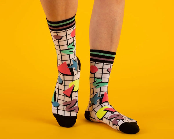 Unisex crew socks with a white and black grid background and neon geometric Memphis Design style pattern. Shown on a model 