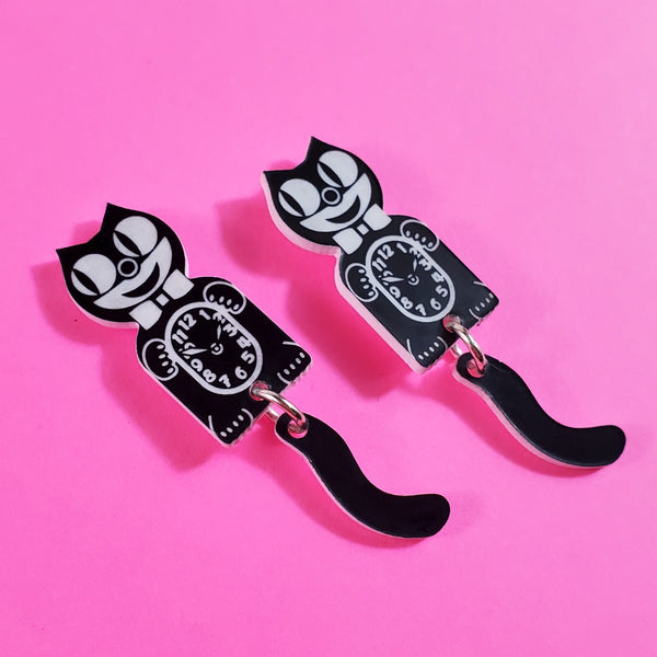 A set of drop earrings in the shape of a pair of Kit Cat clocks with dangling tails. In black