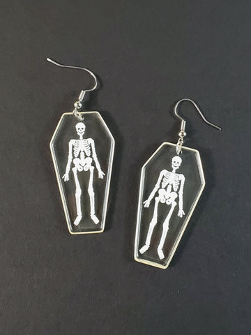 pair of lightweight crystal clear acrylic coffin dangle earrings with white skeletons printed on one side
