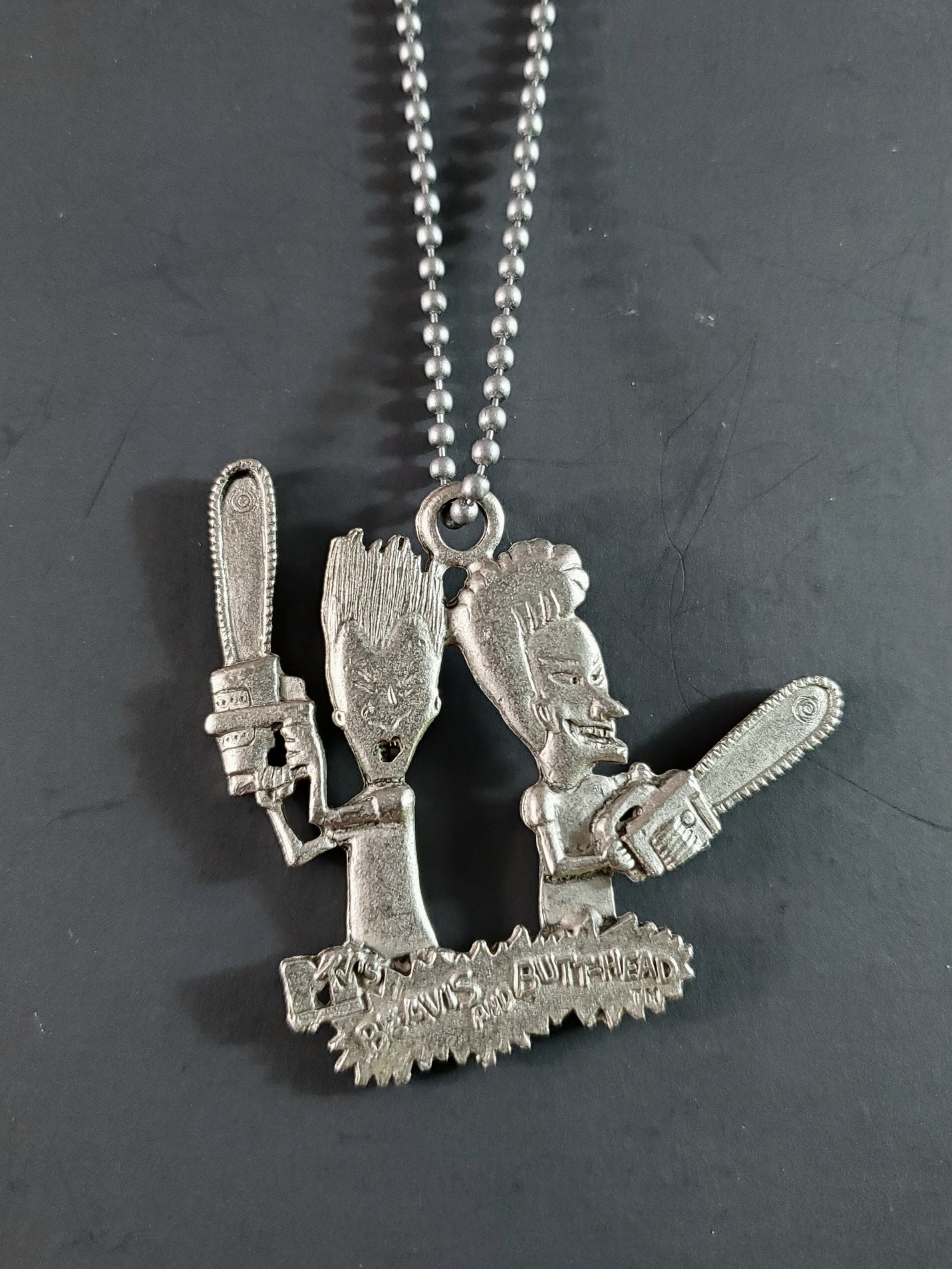 Beavis and Butt-Head deadstock necklace featuring pewter pendant of the duo wielding chainsaws strung on 26" ballchain
