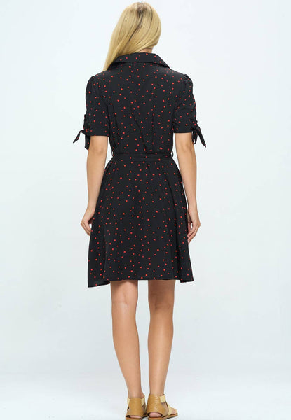 button-front shirtwaist dress in black with allover red heart dot print, featuring notched collar v-neckline, puffed shoulder short sleeves finished with a tie closure detail, self sash belt, and just above the knee flared skirt, shown back view on model