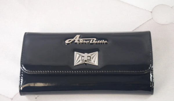 A rectangular tri-fold wallet with a shiny black vinyl exterior. It t has a large silver Astro Bettie logo on its exterior with a silver metal clasp in an Art Deco style