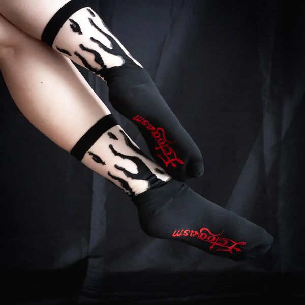 A pair of crew socks with a black flame design & a black cuff, toe, and heel and the Ectogasm logo woven onto the bottom of each sole. Shown on a model without shoes, at an angle to show the red logo