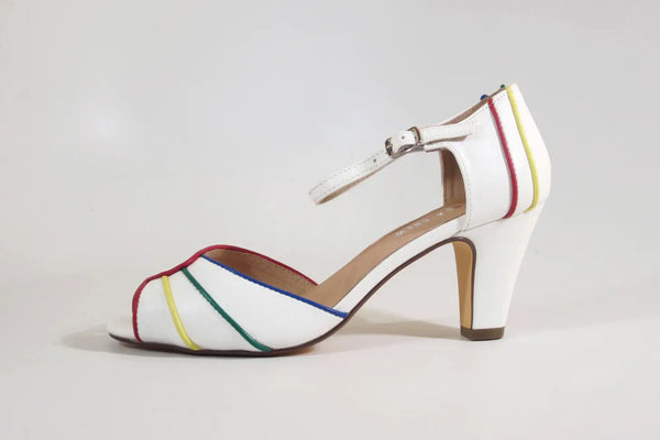A white pair of peep toe heels with red, yellow, green, and blue piping around the edges of the shoe and back of heel. It has a silver metal buckle on the strap. Shown from the side