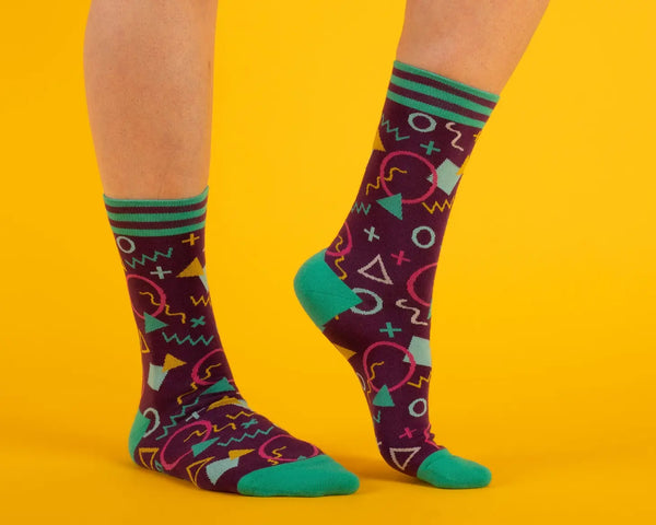 Unisex crew socks in a geometric 80s pattern on a purple background. Shown on a model from the side