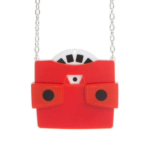 A layered acrylic necklace in the shape of a view finder toy with a red body and black eye holes. It has a white and black view finder reel poking out of its top. On a silver plated curb link chain