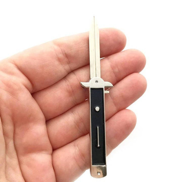 shiny silver metal and black enamel switchblade stiletto knife lapel pin with retractable blade, shown held in a hand