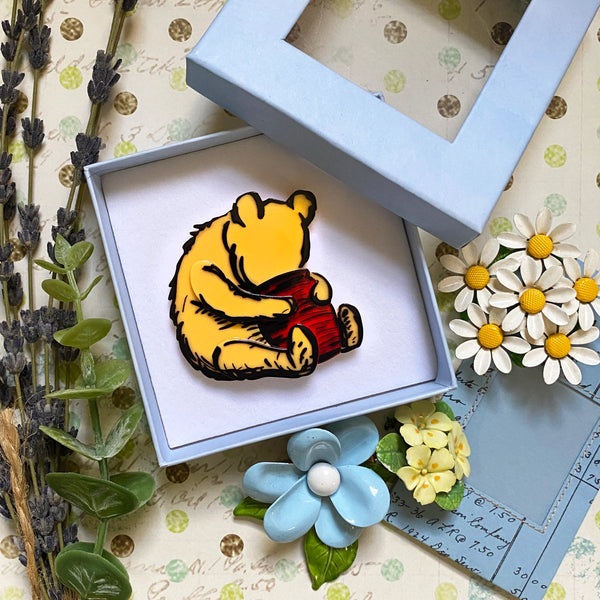 The brooch displayed in its blue gift box in front of a floral background