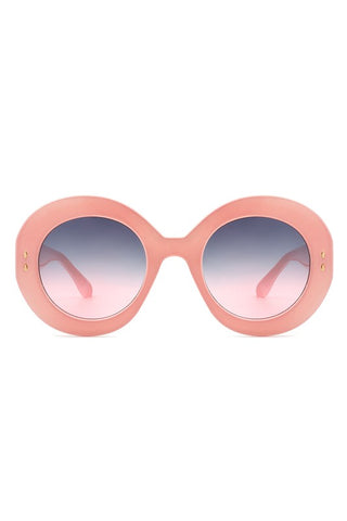 A pair of pink oval sunglasses with smoke to pink gradient lenses and gold detailing on the temples