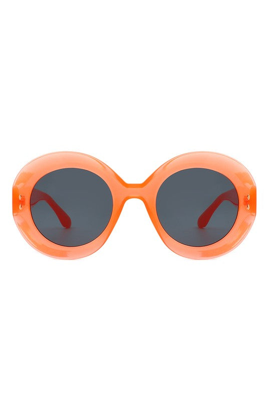 A pair of semi translucent orange oval sunglasses with smoke lenses and gold detailing on the temples