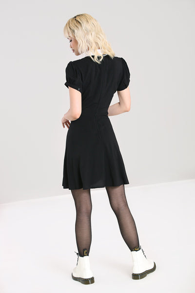 A shirtwaist mini dress with a white pointed collar that has stylized snake embroidery on each side. The dress has a black velvet bow tied around the neck and pin tuck details down the bodice in between the buttons. The sleeves are short and slightly puffed. Shown on model from behind to show zipper in back 