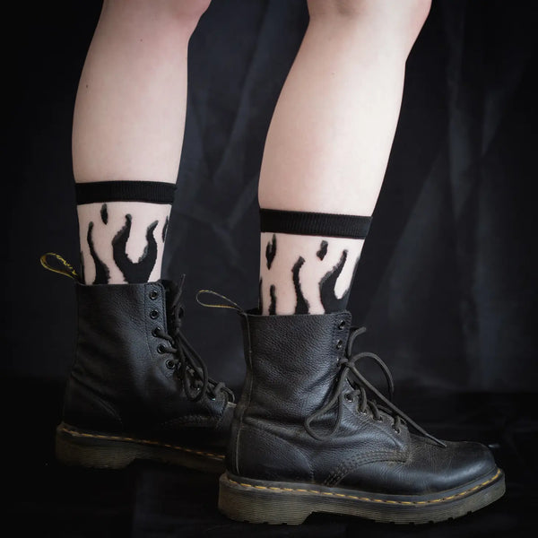 A pair of crew socks with a black flame design & a black cuff, toe, and heel and the Ectogasm logo woven onto the bottom of each sole. Shown on a model wearing Doc Marten boots