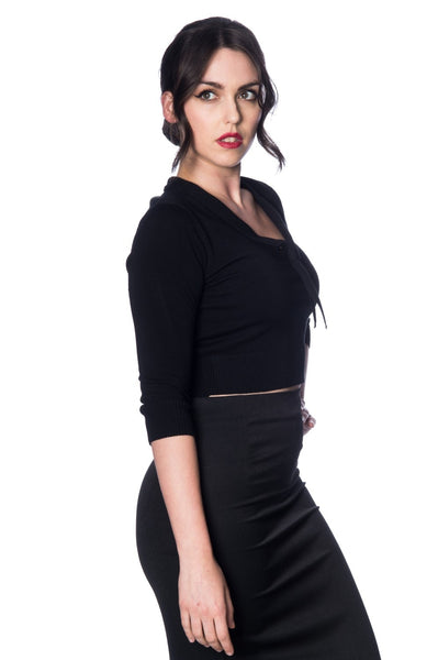 A model wearing a cropped black knit sweater with a v-neck that extends into a tie detail. It has ribbed sleeve cuffs and waist band. Seen from a 3/4 angle