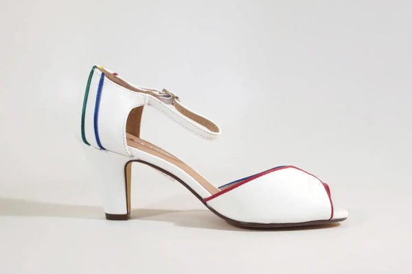 A white pair of peep toe heels with red, yellow, green, and blue piping around the edges of the shoe and back of heel. It has a silver metal buckle on the strap. Shown from the inner side