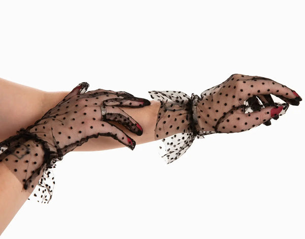 Black mesh wrist-length gloves in a classic flocked dot pattern with a matching ruffled cuff. Shown on a model in close up