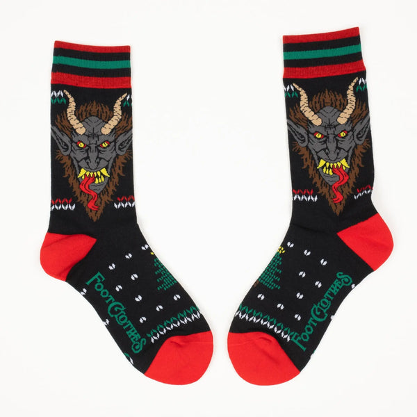 Fair Isle style pattern in red and green of holly and Christmas trees with an illustration of Krampus on soft black stretch cotton blend crew socks. Shows mirrored pattern of both socks