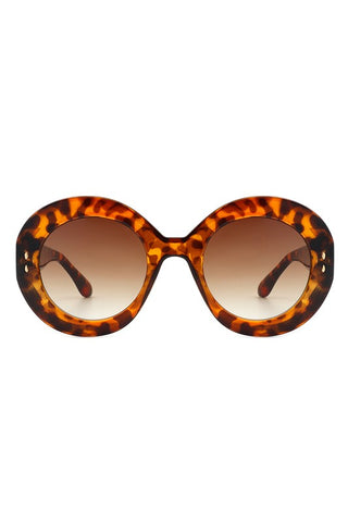 A pair of semi translucent tortoiseshell oval sunglasses with brown gradient lenses and gold detail on the temples