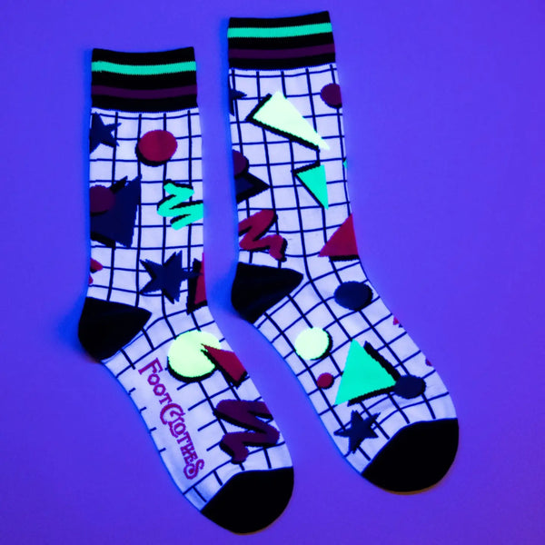 Unisex crew socks with a white and black grid background and neon geometric Memphis Design style pattern. Seen under a UV light