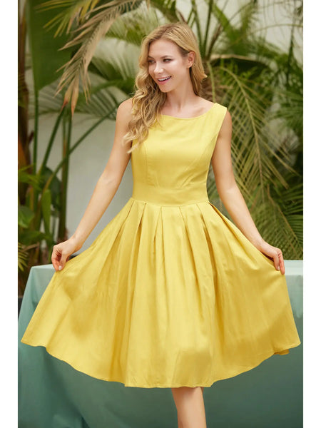 A model wearing a sleeveless dress in a shade of golden yellow with a fitted high neckline and princess seamed bodice, wide banded waist, full box-pleated just below the knee length skirt. Model is holding the skirt of the dress wide to show pleats