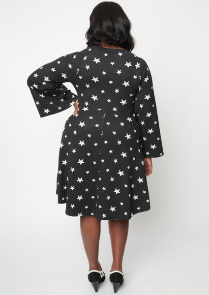 A black sweater knit fit and flare dress with raglan bell sleeves in a black and white star pattern. Shown from behind on a model