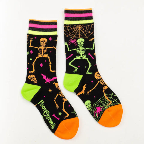 A pair of black crew socks with neon striped black, yellow, orange, and pink cuffs and orange toes. The body of the sock has a pattern of neon colored dancing skeletons, spiderwebs, bats, and spiders. The socks glow in the dark