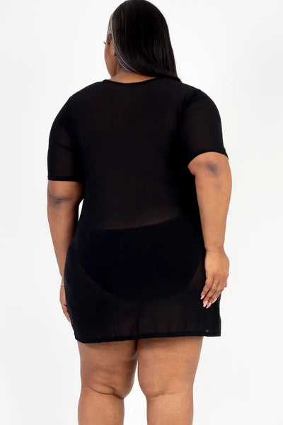 A plus size model wearing a short sleeved black mesh mini dress. Shown from behind 