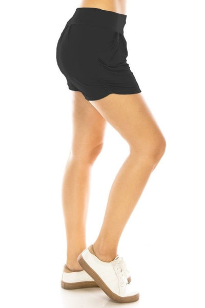 A model wearing black knit shorts with elastic waist band, pleated front, ruched side seam detail, and pockets. Seen from side