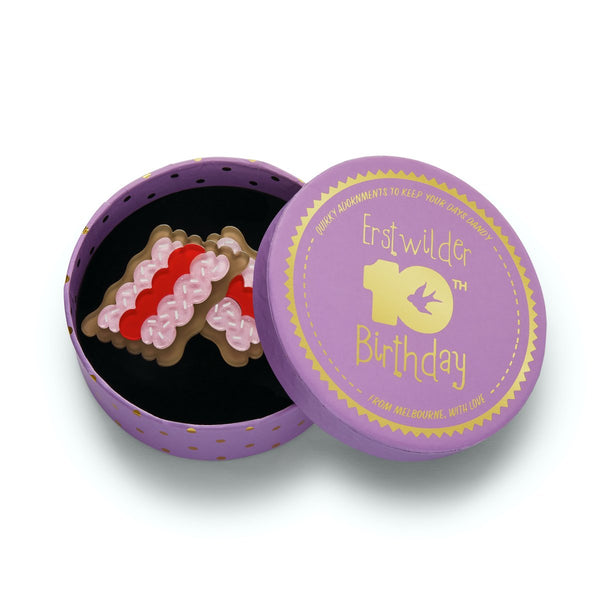 two "Vovos" pink frosting, red jam, and white sprinkles topped biscuits layered resin brooch, shown in illustrated round box packaging