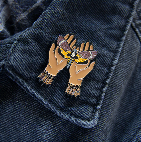 yellow, and brown Death's Head Moth gently held in witchy hands enameled metal double clutch back fastener pin, shown on denim jacket